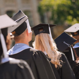 master degree in uae Graduates in caps and gowns stand together, with sunlight illuminating their hair and the blurred background of a campus.