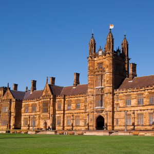 Historical sandstone building of a university, featuring ornate towers and a bright blue sky in the background.